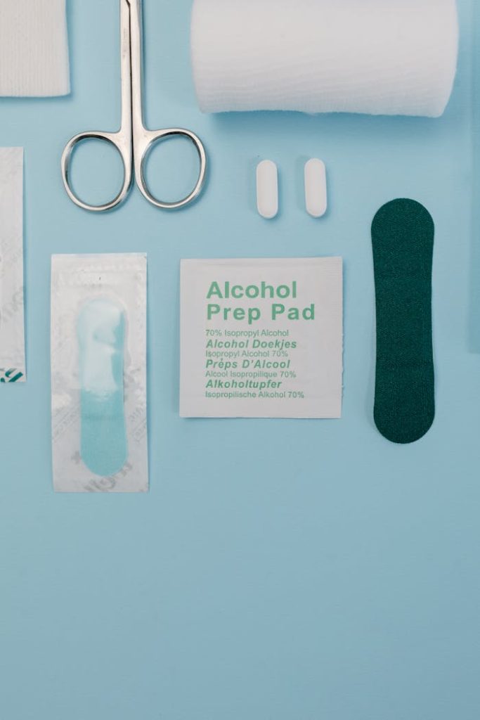 Top view of medical supplies including gauze, scissors, and alcohol prep pad on blue background.